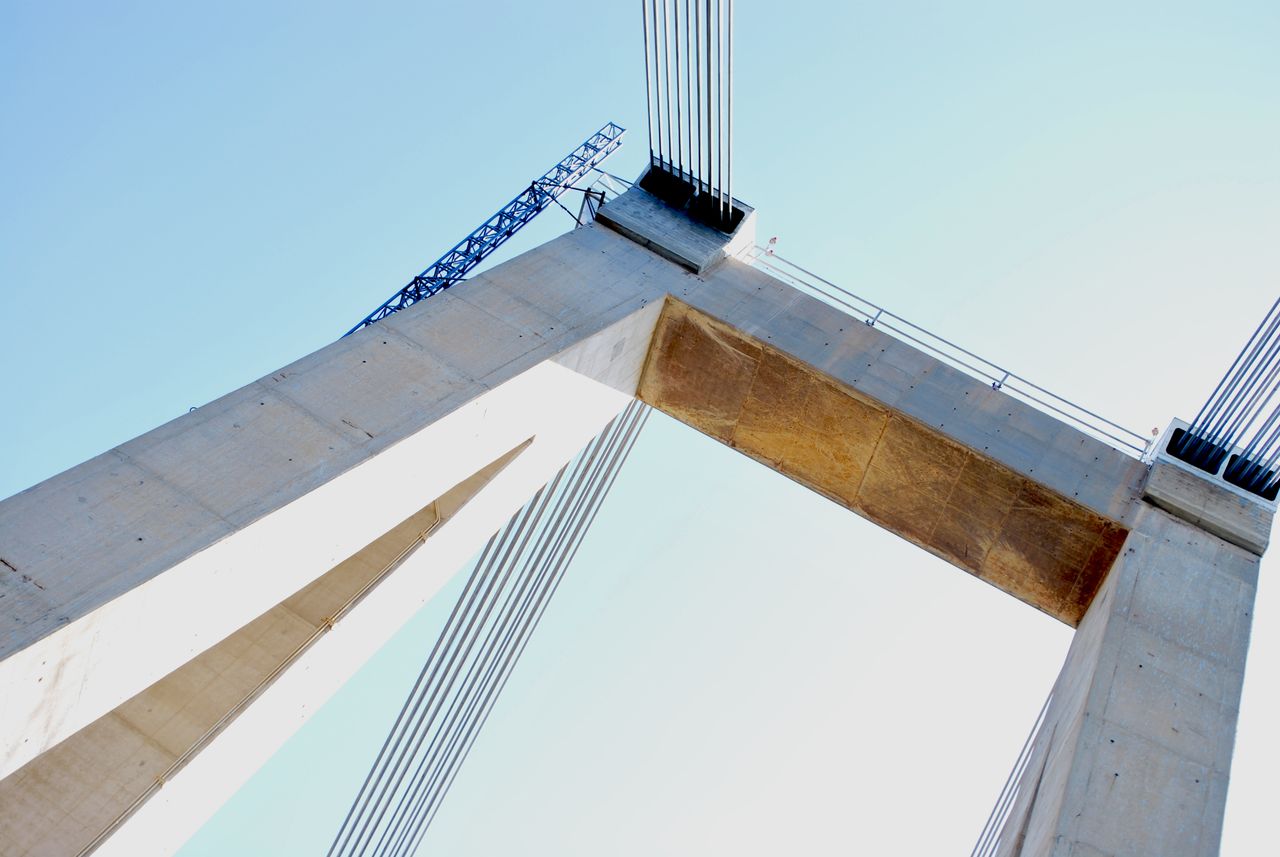 Low angle view of a modern suspension bridge with concrete structure and cables against a clear blue sky.