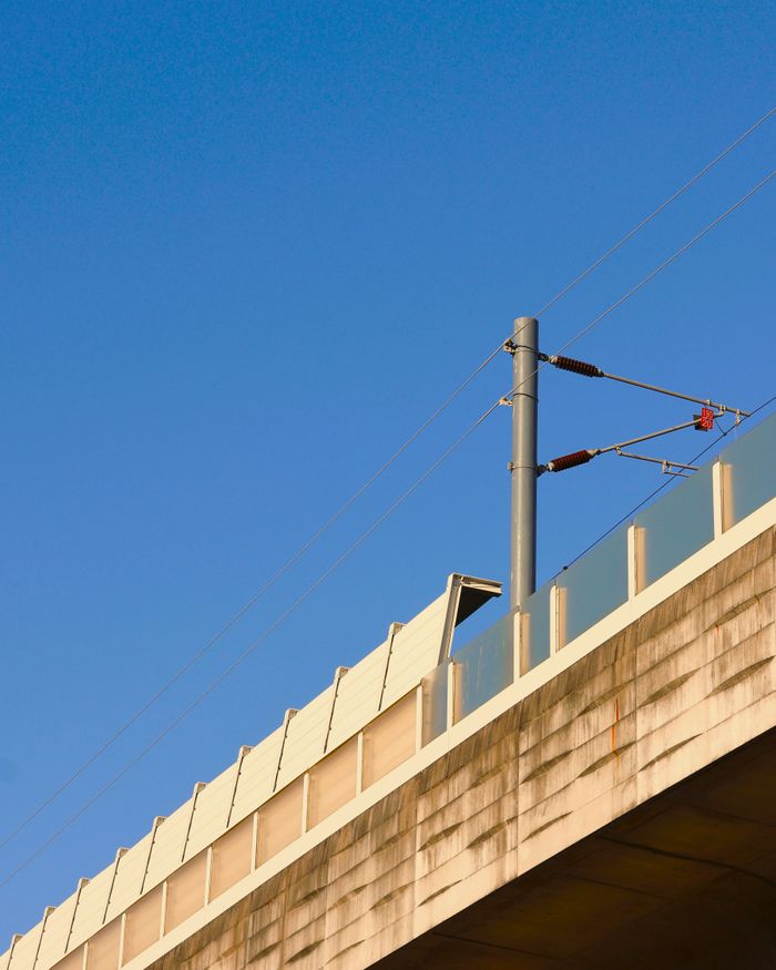 Elevated bridge structure with power lines against a clear blue sky, captured in a minimalist style.