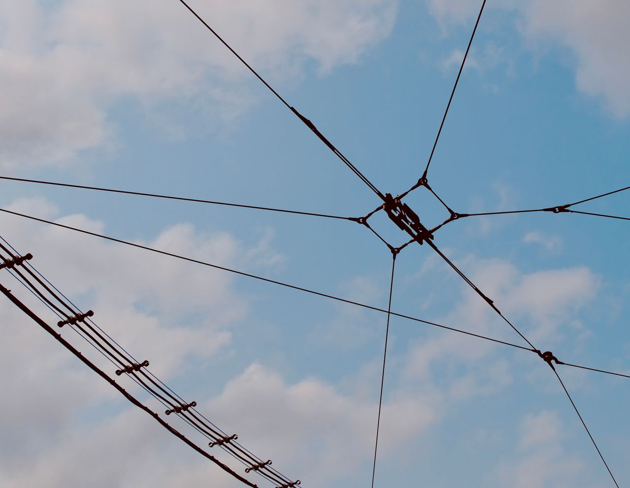 A network of power lines stretching across a blue sky with clouds.